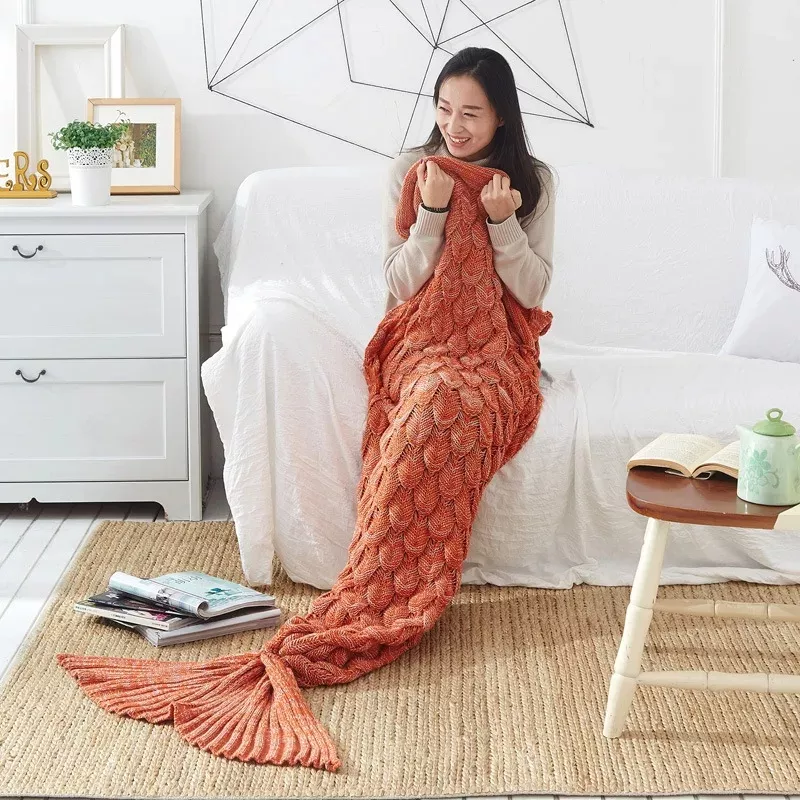 Smiling woman with mermaid tail blanket on sofa.