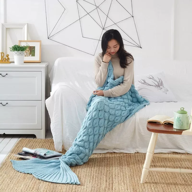 Woman cozy in blue mermaid tail blanket.