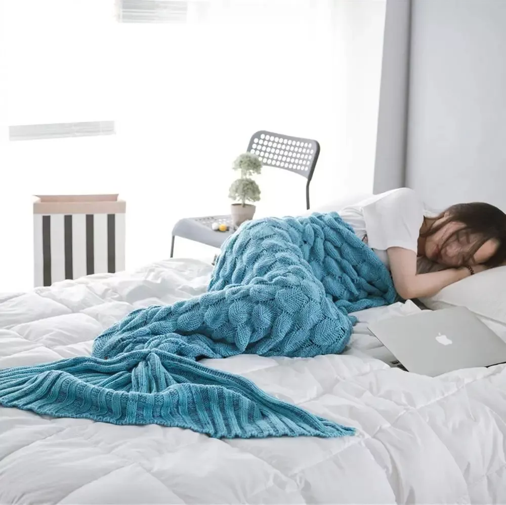 Woman sleeping under blue mermaid tail blanket on bed.