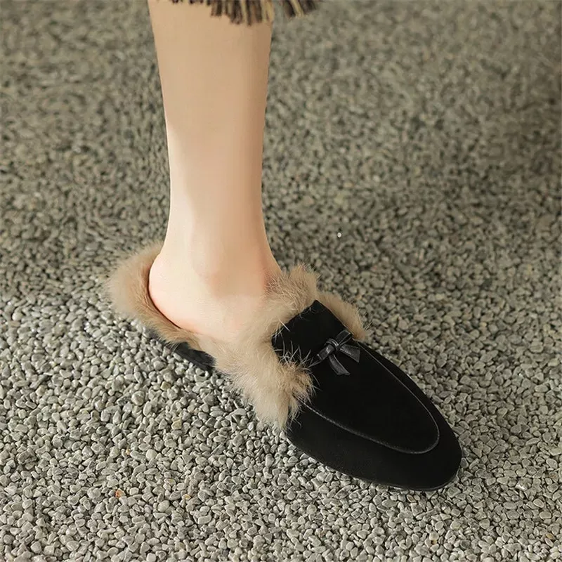 Person wearing black fuzzy slippers on gravel